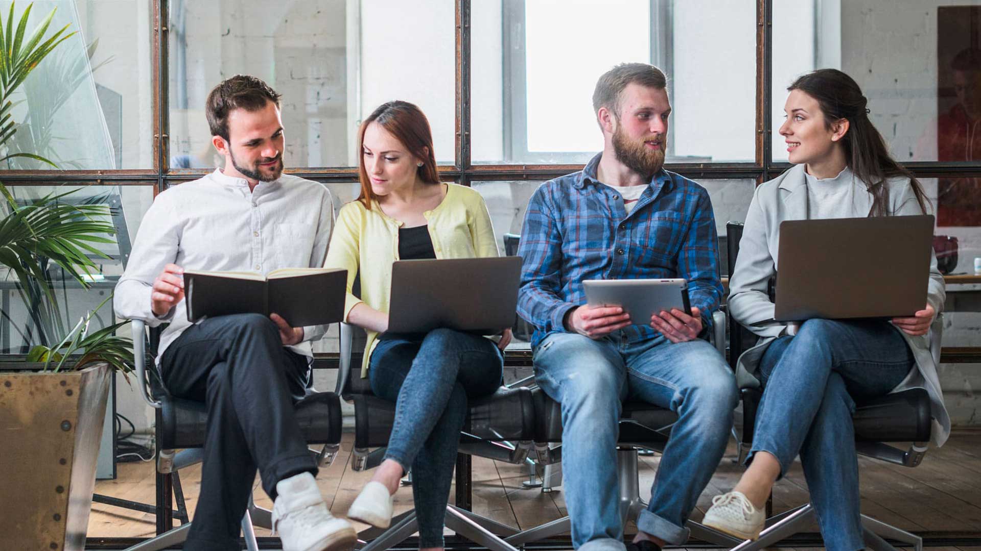 Eine Gruppe von 4 Menschen sitzt und arbeitet nebeneinander mit ihren Notebooks.